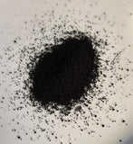 A small mound of Iron Chelate, dark black powder or granules, scattered in a circle on a white plate.