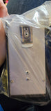 A rectangular silver metal device wrapped in clear plastic, held by a hand over dark blue denim fabric.