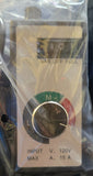 A small industrial control module or switch in its clear plastic packaging, held against blue denim jeans. The device has a white faceplate with a black rotary switch, green and red markings, and printed specifications.