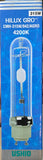A hand holding a Ushio Hilux Gro 315W 4200K AGRO fluorescent light bulb in its blue retail packaging, with a store shelf visible in the background.